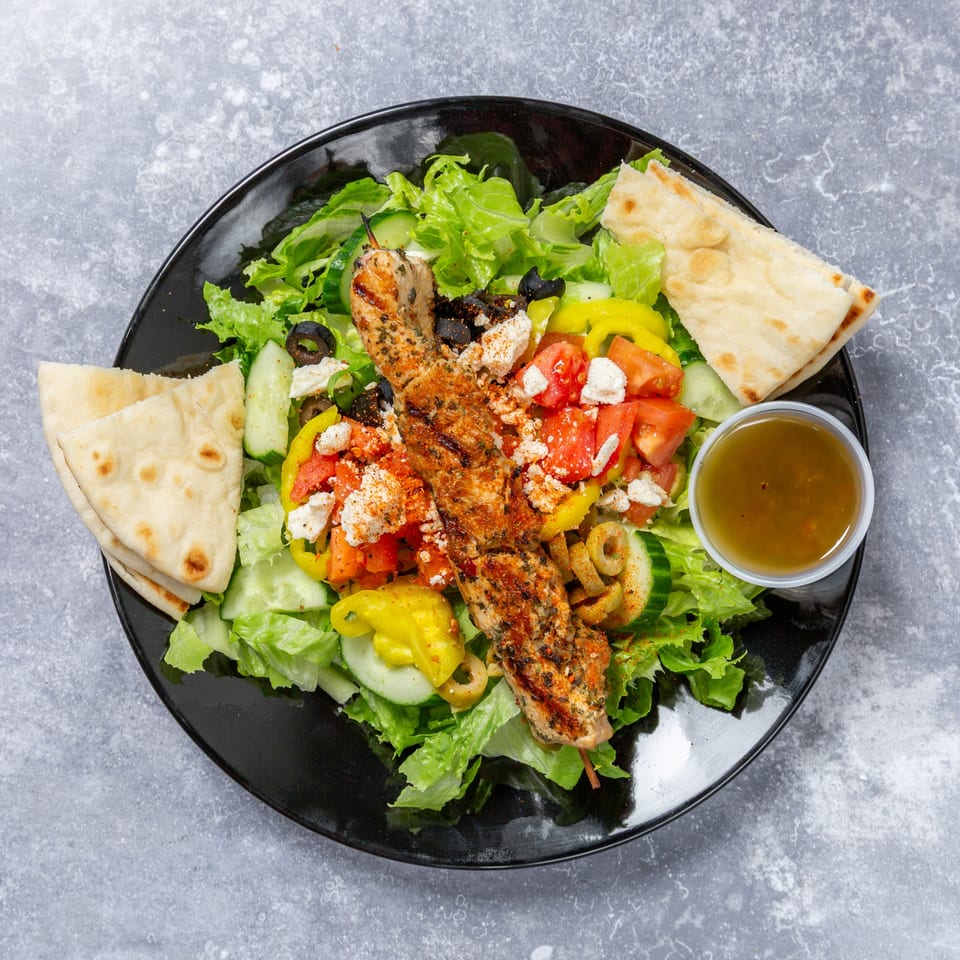 Taza Grill's chicken shish tawook skewer on a fresh Mediterranean salad with pita bread and dressing.
