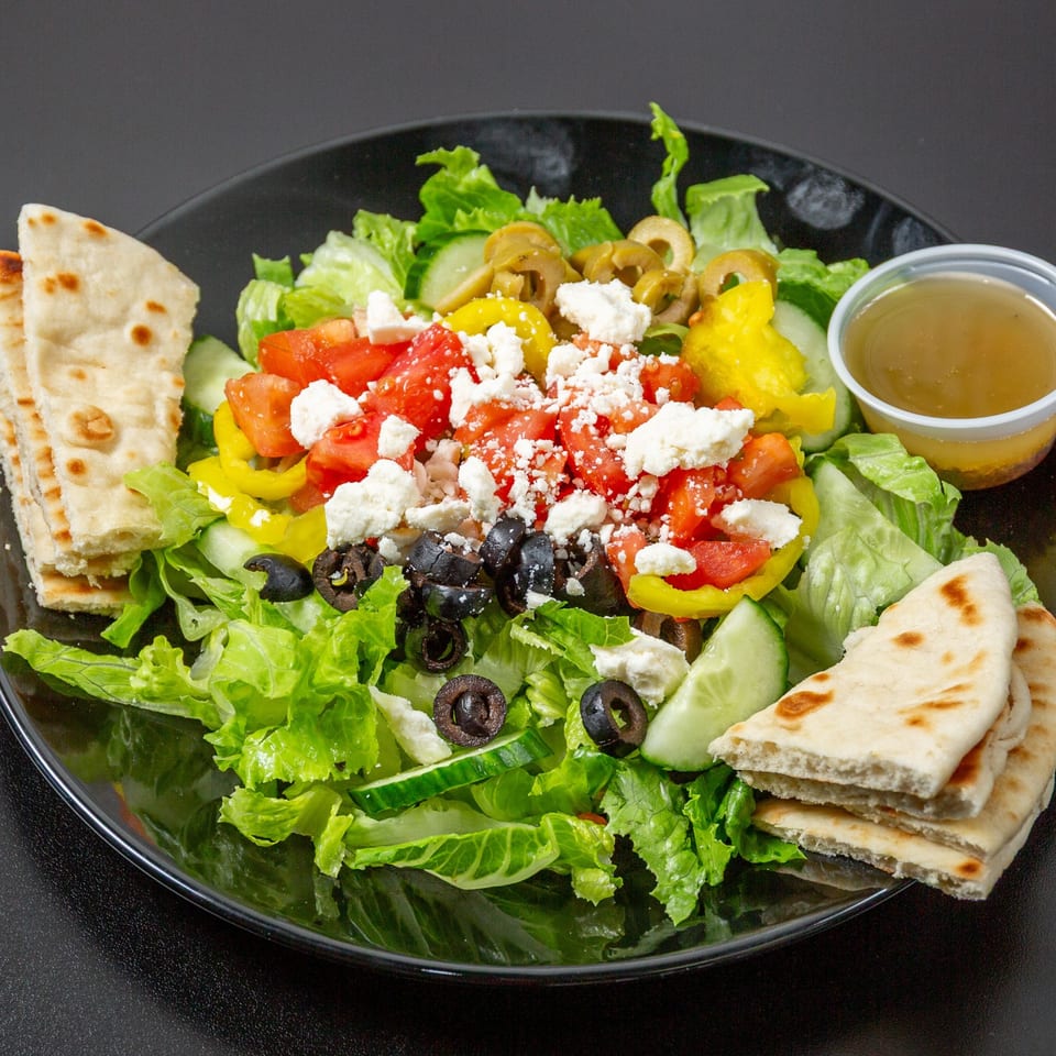 A vibrant Taza Grill Mediterranean salad with feta, olives, tomatoes, and pita bread.