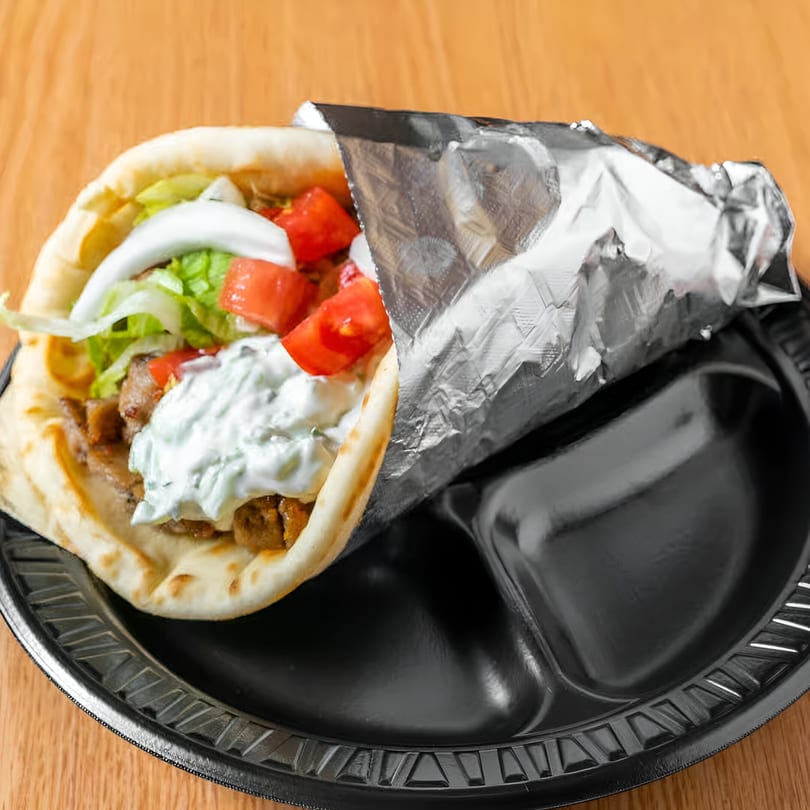 A Taza Grill gyro, wrapped in foil, filled with meat, lettuce, tomatoes, onions, and tzatziki sauce.