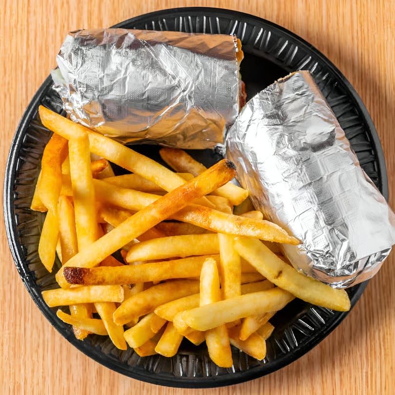 Two foil-wrapped Mediterranean burritos and a pile of golden french fries on a black plate.