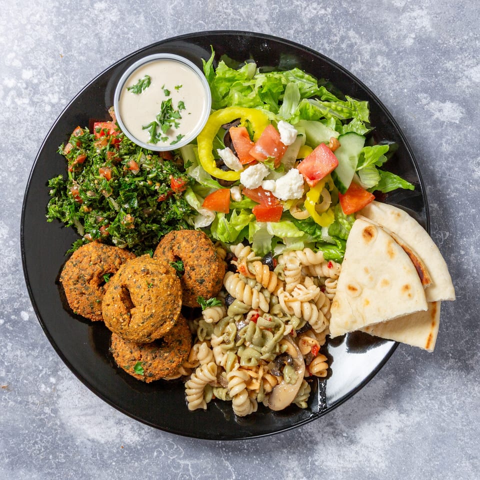 A Taza Grill Mediterranean platter with falafel, tabbouleh, Greek salad, pasta salad, pita, and tahini.