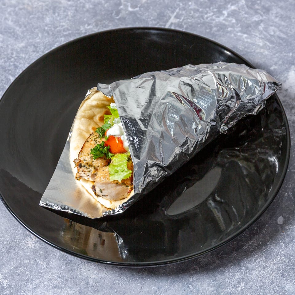 Taza Grill's chicken shawarma wrap, partially unwrapped from foil, on a black plate.