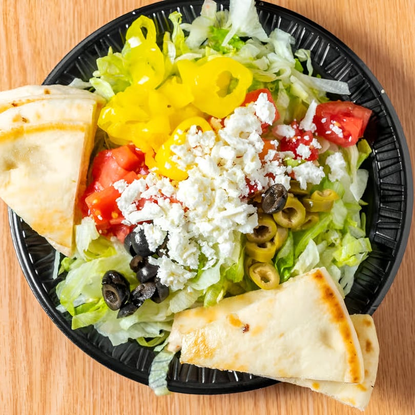 A Mediterranean salad with lettuce, tomatoes, olives, feta, and banana peppers, served with pita bread.